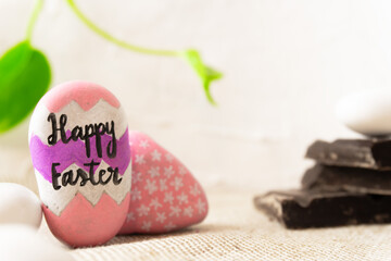 Easter background rocks painted by hand, sentence Happy Easter. blocks of chocolate vibrant green leaves in background
