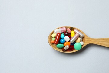 Various pills in wooden spoon on gray background