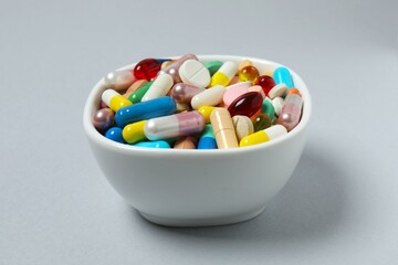 Various pills in a bowl on gray background
