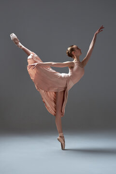 Elegant ballerina in peach dress performs arabesque pose on pointe shoes