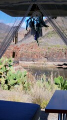 Dream catcher and wind chimes hanging inside a camper van, overlooking a volcanic landscape with a lake and cacti in the Canary Islands, creating a peaceful and relaxing atmosphere