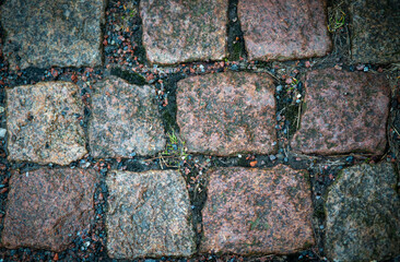 Photo of old cobblestone pavement made of square granite stones. The stones vary in color from gray...