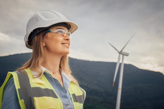 An empowered female engineer in renewable energy, overseeing wind turbines to harness clean energy and promoting environmental awareness and sustainable practices in her community