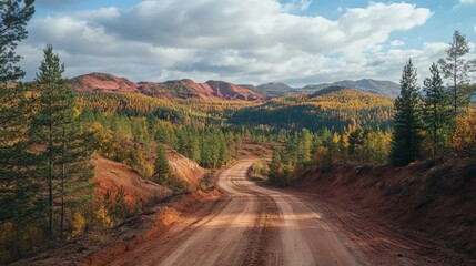 Scenic dirt road through autumn forest and red clay hills with distant orange hued mountains