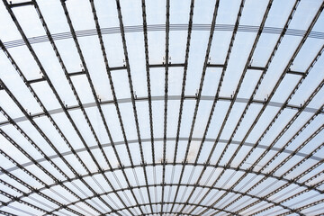 Curved steel framework with glass panels forming a ceiling structure, viewed from below, showcasing architectural design concepts