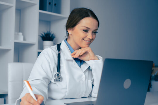 A doctor holds a virtual consultation, showcasing modern healthcare. With a laptop and stethoscope, the physician takes notes and smiles, illustrating telemedicines importance in wellness