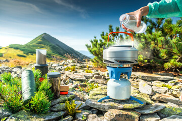 Fototapeta premium Close-up of woman pouring water into kettle on portable stove in alpine campsite