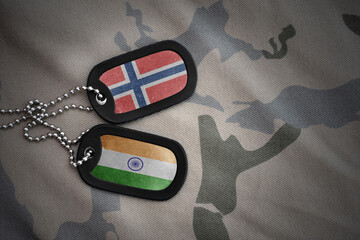 vintage army blank, dog tag with flag of norway and india on the khaki texture background. military...