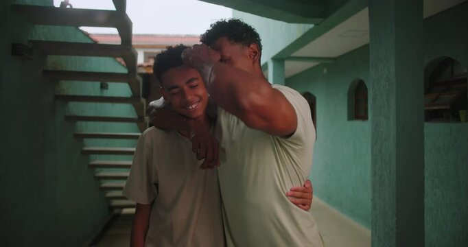 Father wrapping arm around teenage son of African descent standing together in a corridor sharing a heartfelt and supportive family moment