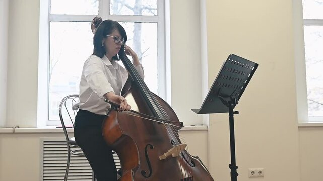 A female musician performs on the double bass in a rehearsal studio. The serene atmosphere complements her dedication to creating rich and harmonious sounds