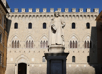 Naklejka premium Siena, SI, Italy - February 20, 2023: Ancient statue and the headquarters of Italian bank called MONTE DEI PASCHI DI SIENA or MPS