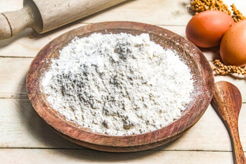 flour in a wooden bowl with eggs and a rolling pin beside it.