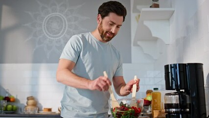 Positive man mixing salad preparing food at cozy kitchen closeup. Guy cooking