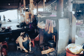 Unidentified Vietnamese lady prepare Com Lam rice in bamboo tube near kitchen smoker with dried buffalo pork beef jerky hanging in Mai Chau, spied dried iron meat hanger on wooden fire, Vietnam
