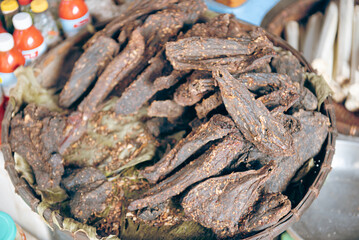 Pile of spiced buffalo jerky snack smoked with Com Lam rice in bamboo tubes and red sauce at traditional restaurant of ethnic people in Mai Chau, Hoa Binh, Vietnam, dried barbeque wooden fire