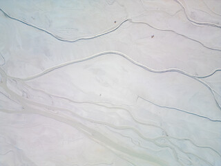 A turquoise tailings pond near a cement factory, surrounded by rugged hills. The vivid water...