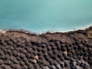 A striking contrast between turquoise water and dark, rugged terrain at a tailings lake. The...