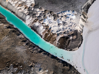 A striking contrast between turquoise water and dark, rugged terrain at a tailings lake. The...
