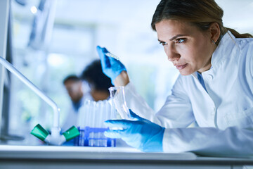 Young female scientist examining chemical liquid in a beaker while working  in laboratory.