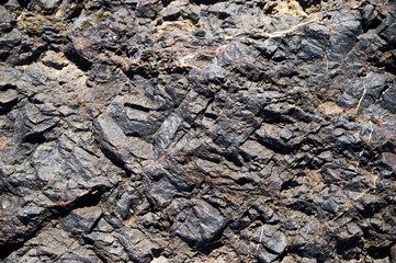 Dark rocky terrain with intricate textures and patterns captured in sunlight by a geological formation in a natural landscape