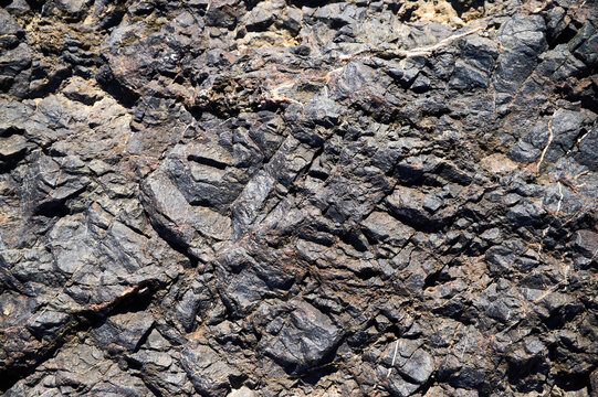 Dark rocky terrain with intricate textures and patterns captured in sunlight by a geological formation in a natural landscape