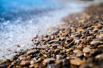 Waves crash on colorful pebbles along a serene beach during the calm afternoon