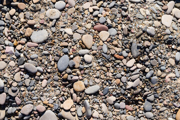 Smooth, colorful pebbles scattered across a sandy beach on a sunny day