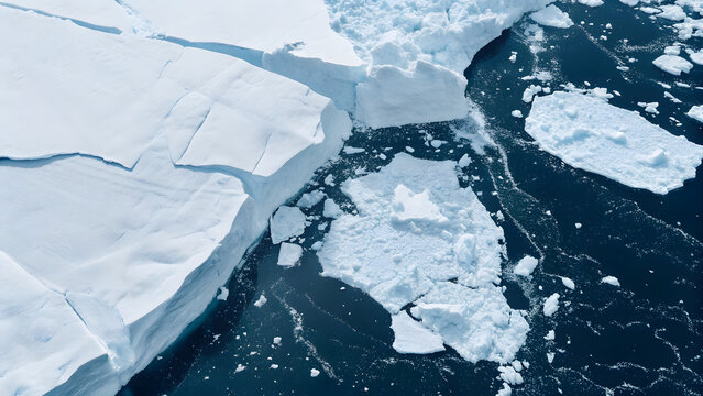 Aerial perspective of icebergs detaching from the glacial wall in Antarctica. Set against a dark blue background, the cinematic composition captures the majesty and drama of the frozen landscape