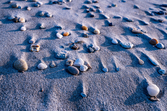 Kleine bunte Steine liegen am Sandstrand, der Wind hat hinter den Steinen Sand angeh&auml;uft