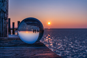 Glaskugel spiegelt eisige Winterlandschaft, Blendenstern der Sonne bei orangerotem Sonnenuntergang,...