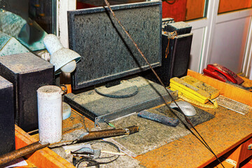 Cluttered office desk covered in a thick layer of dust and debris, after a fire disaster. Desk contains a computer monitor, keyboard, speakers,  telephone,  various office supplies, all are damaged 