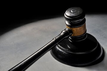 A gavel on a surface illuminated by a single light source, casting a dramatic shadow. Justice and...