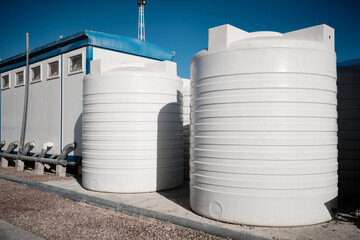 White plastic water tanks stands next to prefabricated industrial toilet containers. Prefabricated...