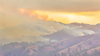 Fototapeta premium A forest fire is raging in the mountains, with smoke and flames rising from the trees on the hillsides. An aerial view of nature in a dangerous condition during the summer season