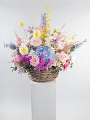 Bright and colorful spring floral arrangement featuring roses, hydrangeas, dahlias, and orchids in a woven basket