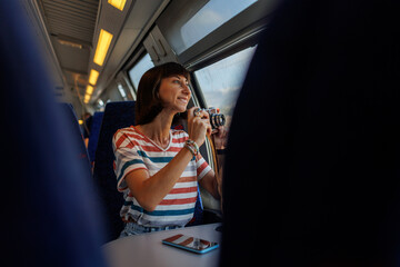A young girl uses a camera to photograph a beautiful view from the window while traveling by train....