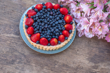 blueberry and strawberry cake and delicate pink alstroemeria flowers on a rough wooden background. copy space 
