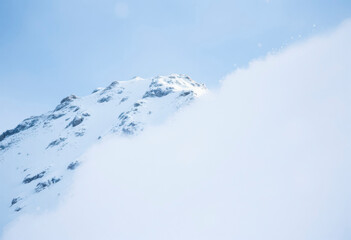 A massive avalanche cascades down the mountainside, displacing snow and creating a dramatic display against a clear blue sky.