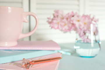 notebooks, cup, diary, delicate pink sakura flowers placed on a pastel blue table. The scene vibrates
calm, style and creativity, ideal for work or creative space.