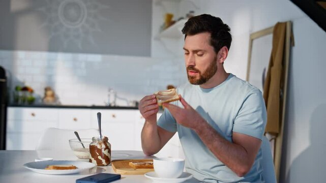Breakfast guy making sandwich at light kitchen closeup. Hungry man eating snack