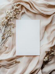 Flat lay of blank white wedding invitation card, surrounded by delicate silk fabric and dried flowers, with neutral color palette. Soft lighting, elegant and sophisticated atmosphere. View from above