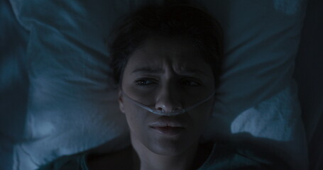 Tired female patient in hospital ward with oxygen tube in nose awaken after sleep.