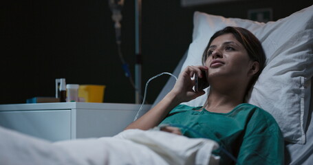 Hospitalized young woman chats on the phone from her bed in the ward.
