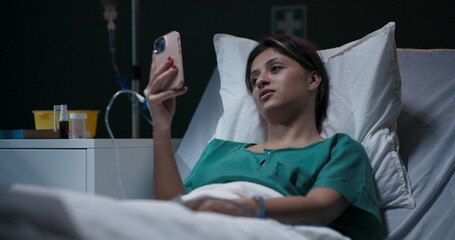 Young patient lies in a hospital room, an oxygen tube in her nose, chatting via video call.