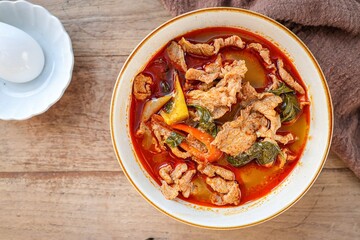 Thai spicy red curry add spicy red curry paste and coconut milk in ceramic bowl on wooden background, thai food, thai cuisine	