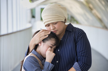 Sad crying daughter staying with her terminally ill mother wearing cancer cap, suffering from...