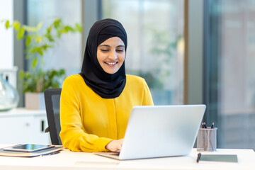 Successful businesswoman in hijab working with laptop inside office at workplace. Arab woman...