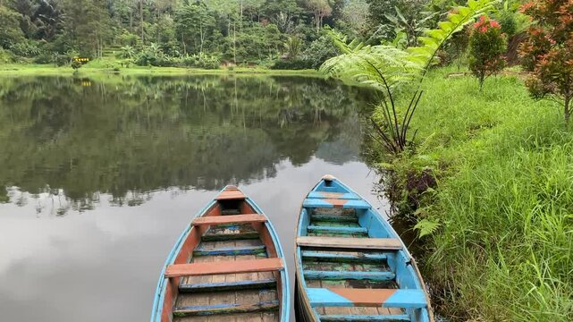 View of Kumpe Lake in Banyumas, Central Java, Indonesia, captured on January 25, 2025. A traditional wooden boat floats on calm waters, surrounded by lush greenery, showcasing Indonesia's serene lands
