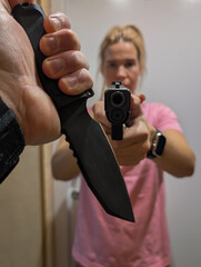 A young blonde girl holds a robber with a knife in his hand at gunpoint. Vertical photo.