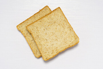 Two slices of wholewheat bread on a white wooden table, showcasing a healthy and nutritious breakfast or snack option with a rustic and simple presentation.